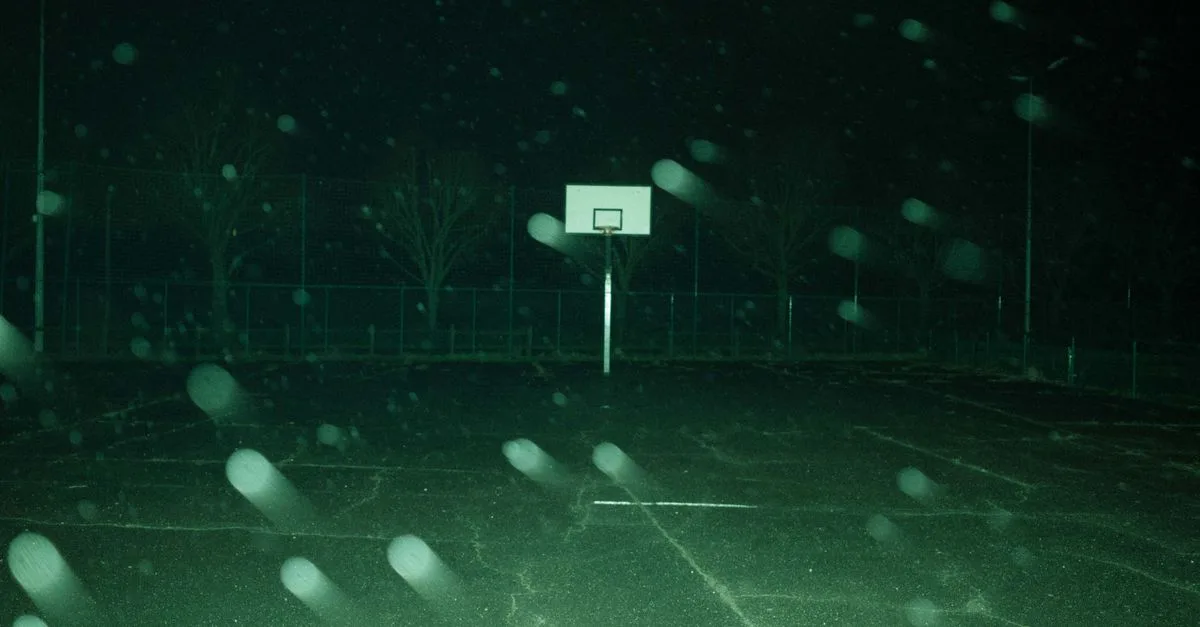 Abandoned basketball court at night with fog creating a moody, eerie atmosphere.