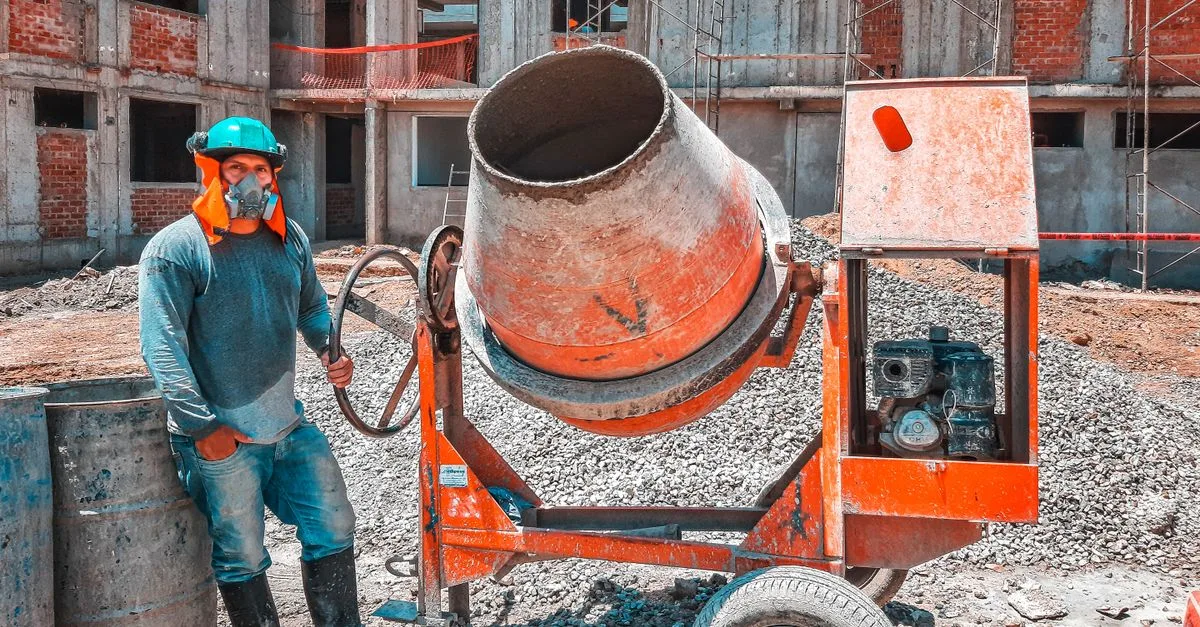 A construction worker operating a concrete mixer at an active building site, emphasizing safety gear.
