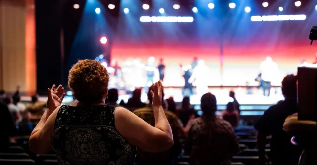 A lively concert setting with an engaged audience clapping, under vibrant stage lights.