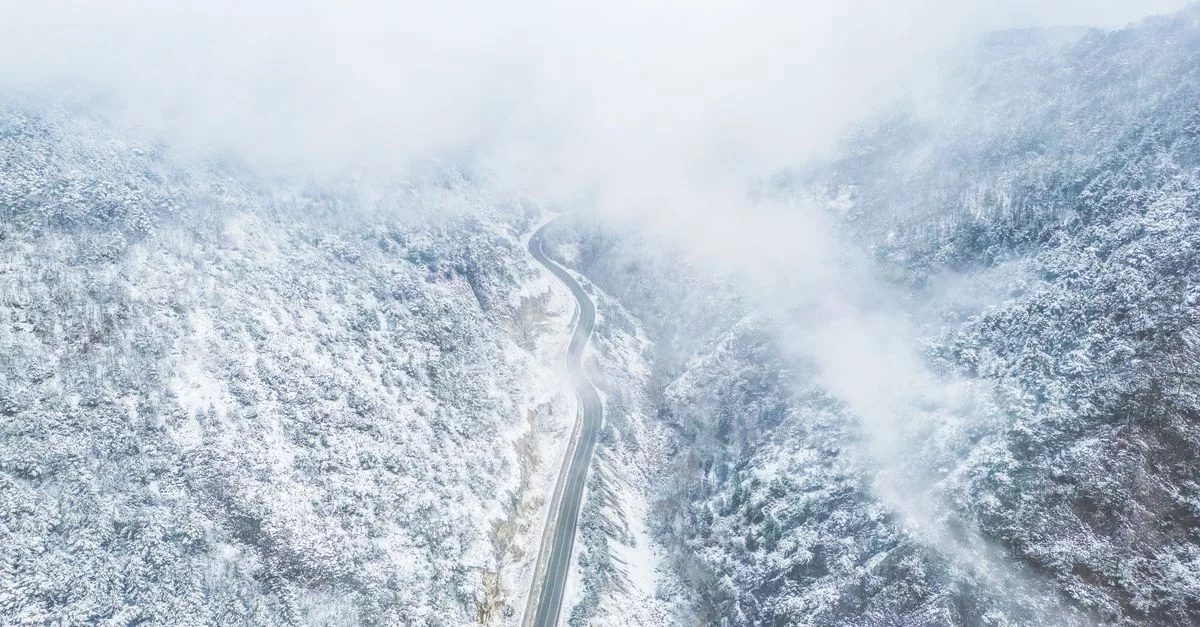 Majestic aerial view of a winding road through snow-covered mountains.