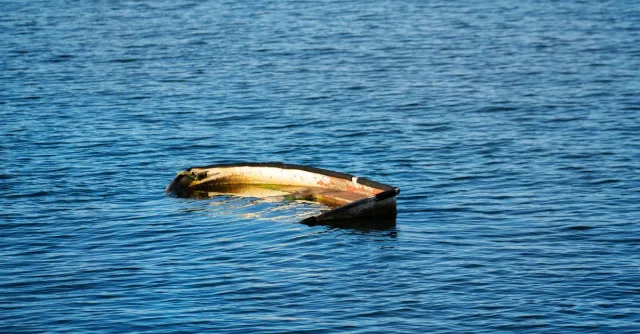 A half-submerged boat floating in a calm sea under daylight, conveying solitude and mystery.
