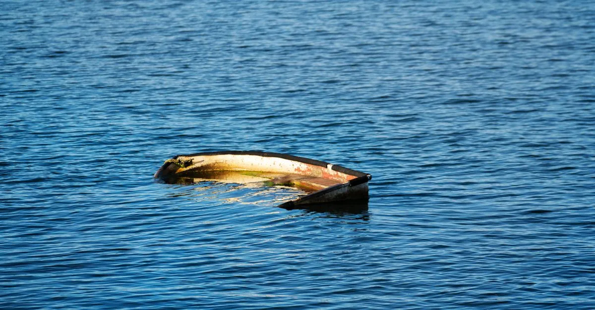 A half-submerged boat floating in a calm sea under daylight, conveying solitude and mystery.