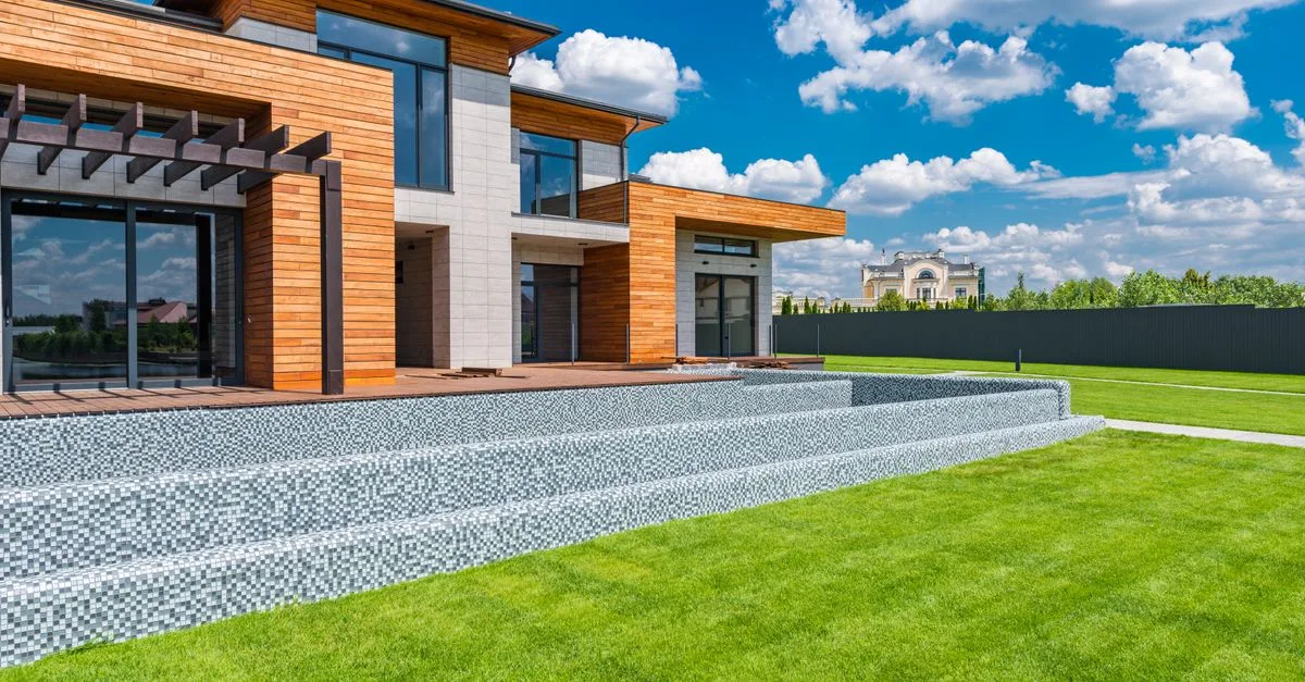 Exterior of contemporary residential house with panoramic windows glass doors and green lawn in yard on sunny day against blue sky with white clouds