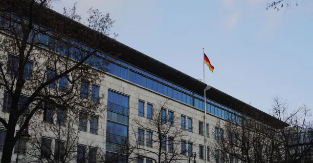 A modern building with a German flag, surrounded by bare trees under a clear sky.
