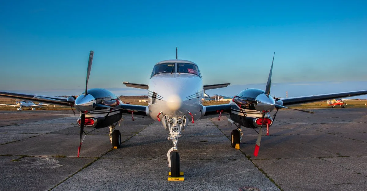 A front view of a twin-engine aircraft on tarmac under clear blue skies.