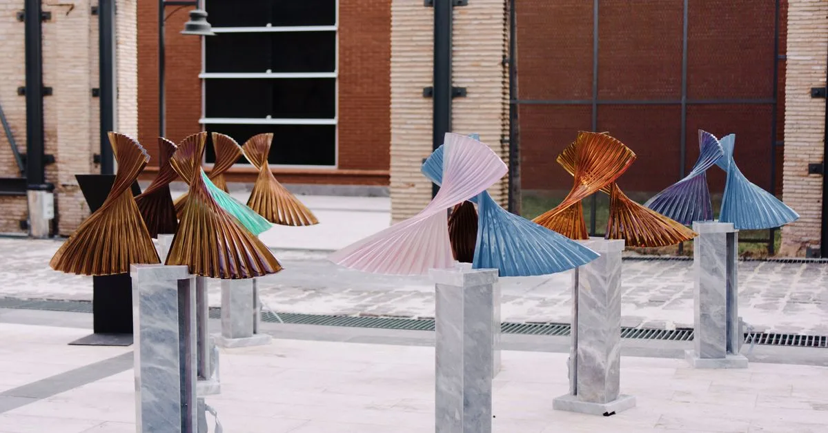 Vibrant metal sculptures displayed on marble stands in an outdoor art exhibit.