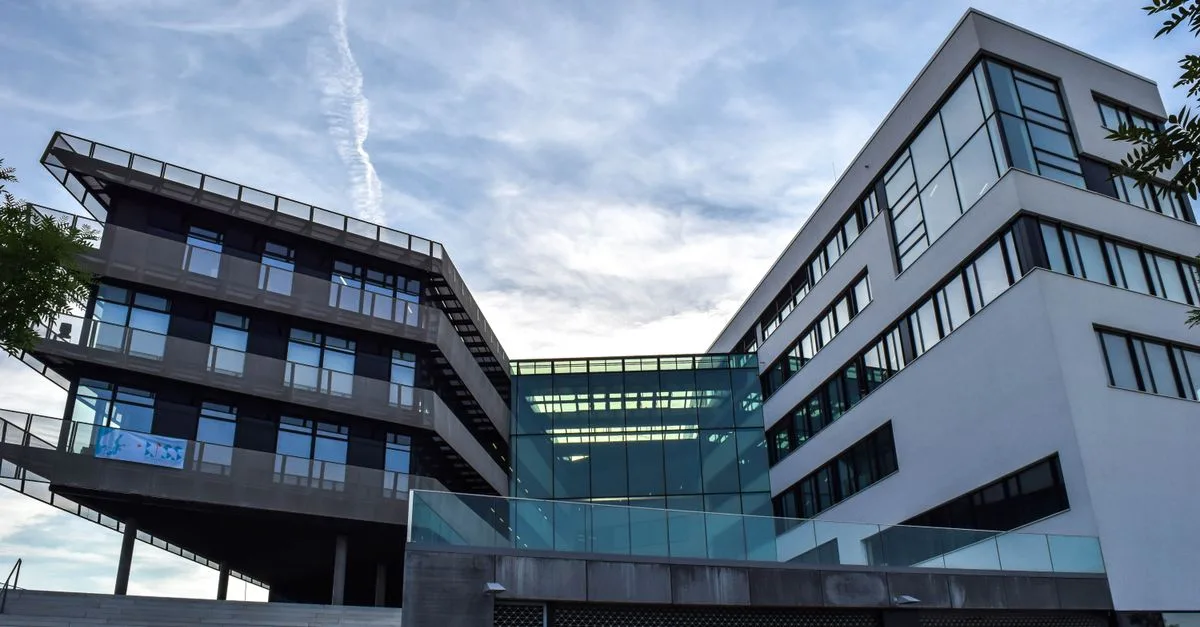 A modern glass-facade building against a blue sky, featuring innovative architecture.