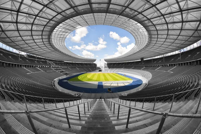 A wide-angle view of a large, empty professional football stadium with green grass and tiered seating.