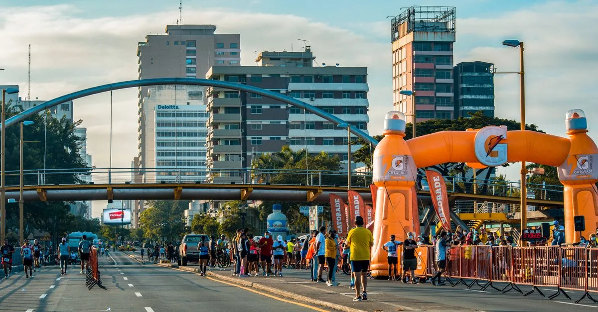 Runners participating in a marathon event amidst a vibrant cityscape under an orange inflatable arch.