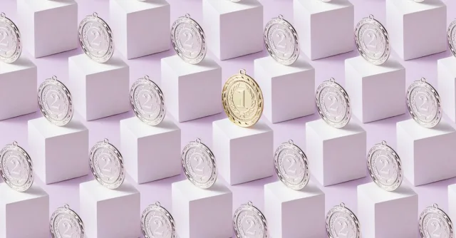 A gold medal stands out among silver medals on white cubes, showcasing uniqueness.
