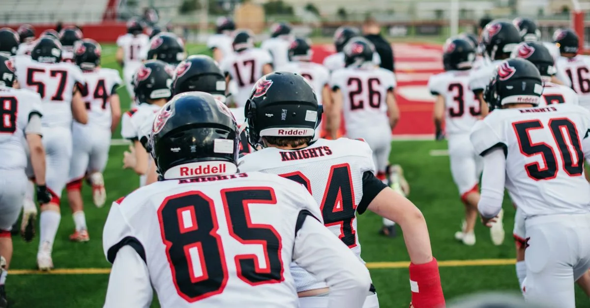 High school football team in uniforms running onto field during practice.