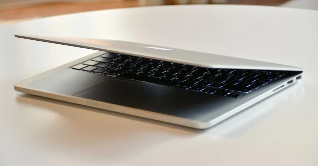 A modern MacBook laptop with a sleek design, slightly closed on a white table indoors.