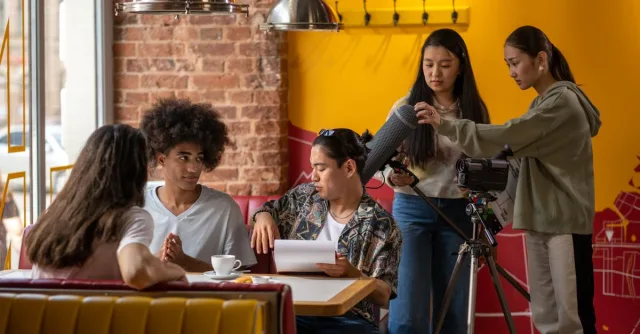 A diverse film crew collaborating in a cozy cafe setting with cameras and microphones.