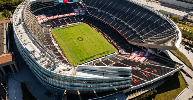 Aerial shot of a modern, empty soccer stadium surrounded by city buildings on a clear day.