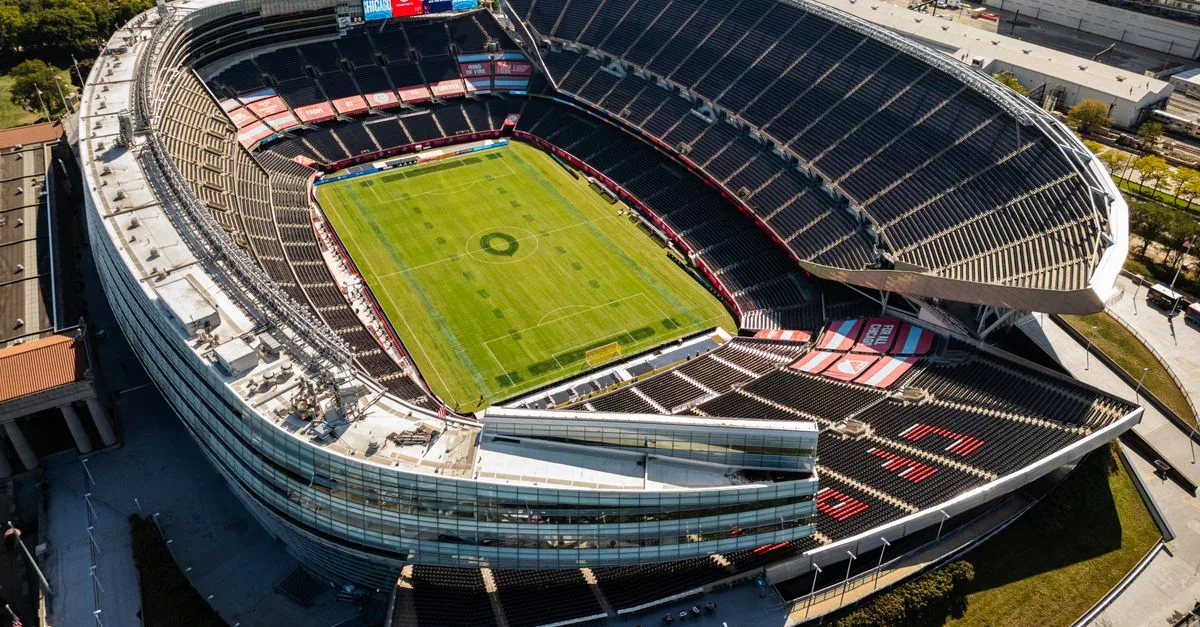 Aerial shot of a modern, empty soccer stadium surrounded by city buildings on a clear day.