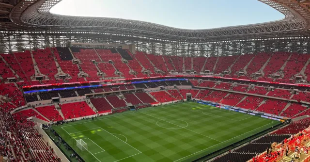 Aerial view of a modern stadium with vibrant red seats and a well-maintained green field.