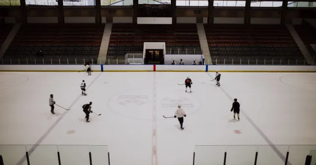 A group of ice hockey players practicing in an indoor rink with empty stands in the background.