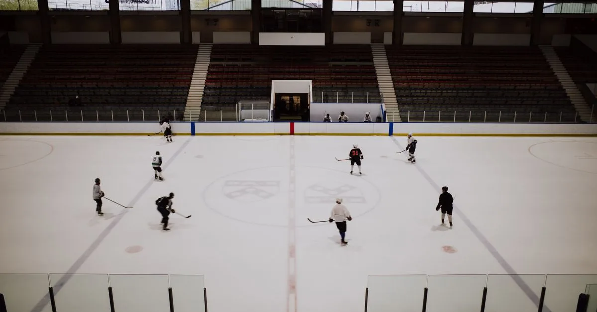A group of ice hockey players practicing in an indoor rink with empty stands in the background.