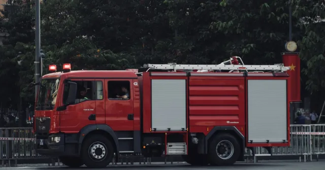 A vibrant red fire truck is parked on a city street surrounded by trees, showcasing urban emergency readiness.