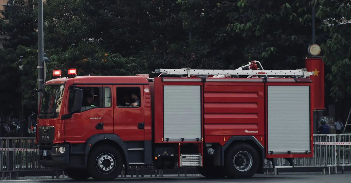 A vibrant red fire truck is parked on a city street surrounded by trees, showcasing urban emergency readiness.