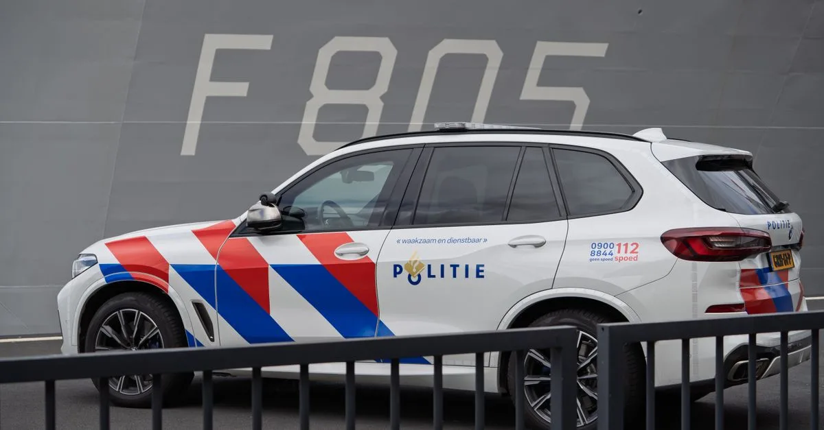 Dutch police SUV parked next to a naval ship marked F 805, highlighting law enforcement and military presence.
