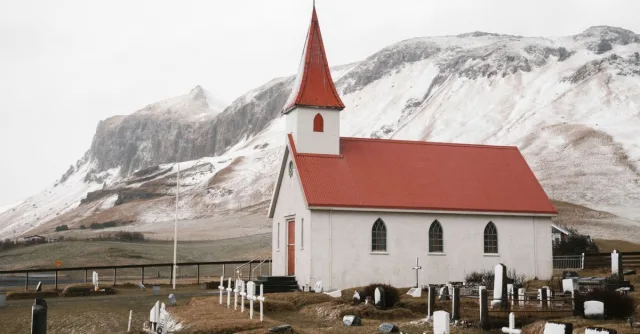 Dyrholaey Church and quiet churchyard with cemetery near magnificent snowy mountains on cloudy autumn day in Iceland