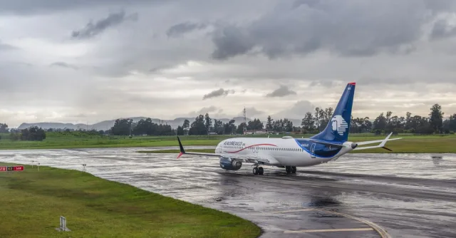 A commercial airplane taxiing on a wet runway under a cloudy sky at an airport.