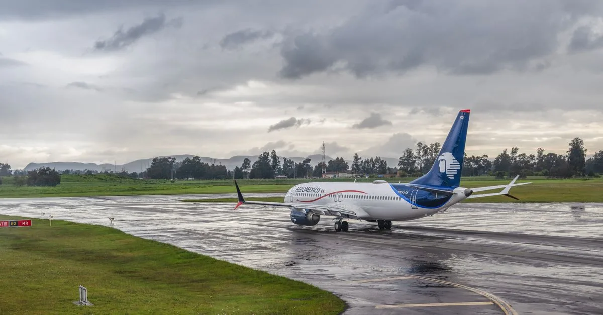A commercial airplane taxiing on a wet runway under a cloudy sky at an airport.