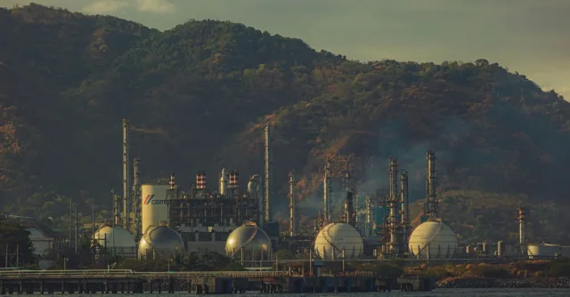 Industrial factory near mountains by a river, showcasing chimneys and infrastructure.