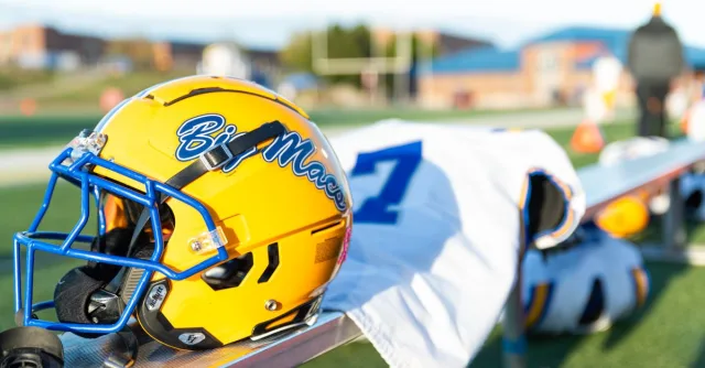 A yellow football helmet with blue highlights rests on a sports bench, ready for the game.