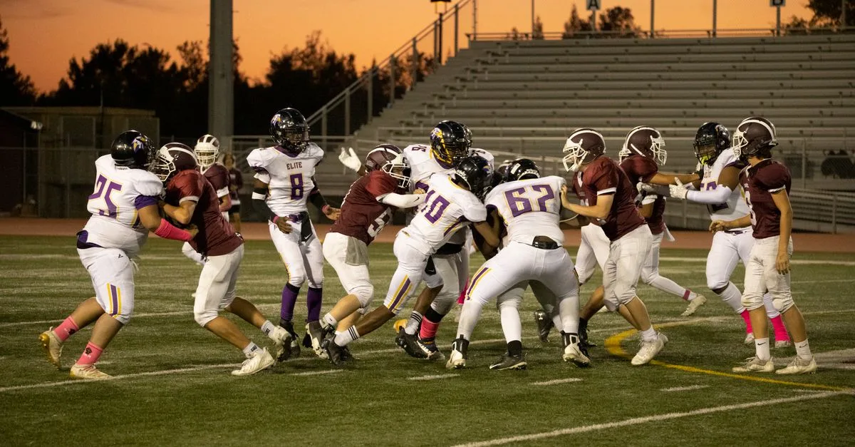 Exciting high school football game with players in action on a field at sunset.