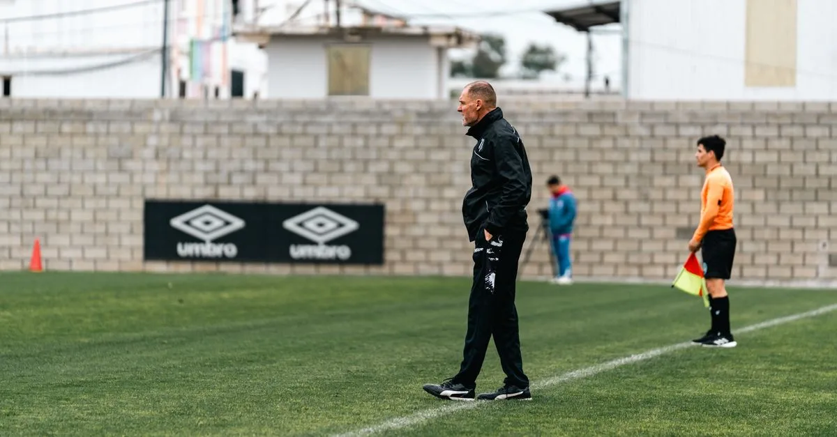 A soccer coach attentively observes a training session, standing by the sideline.