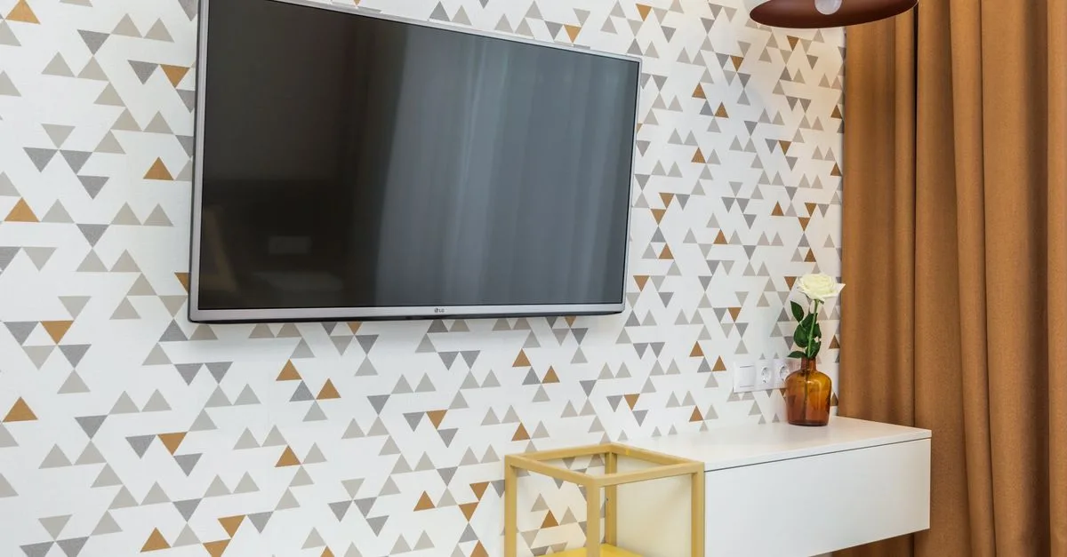 Elegant room interior featuring a TV, geometric wallpaper, and a flower vase.
