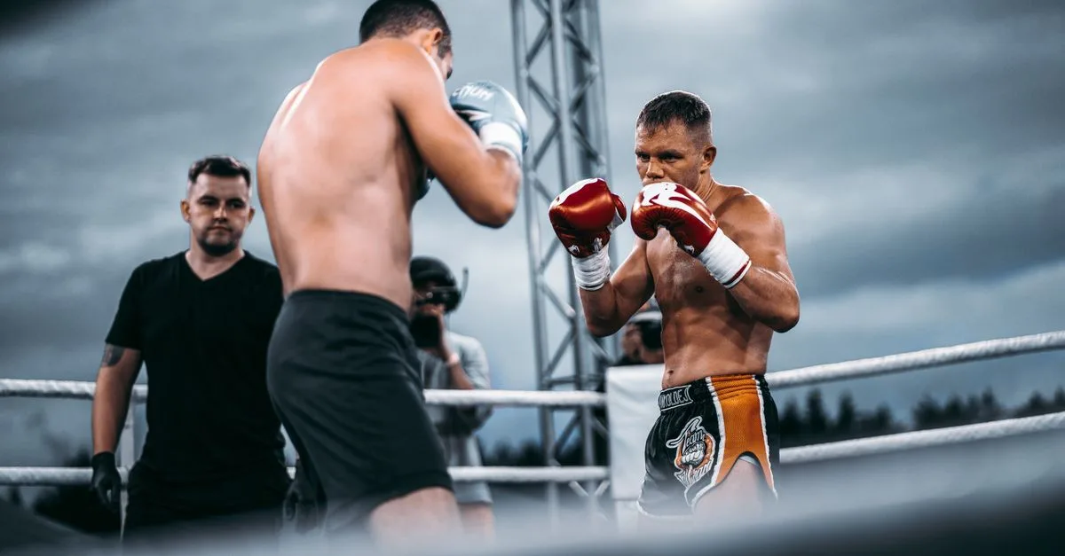 Two men sparring in an outdoor boxing ring under a cloudy sky, showcasing intense focus and athletic prowess.