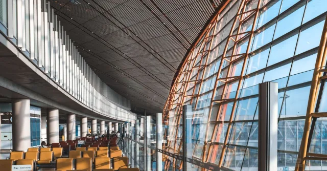 Interior view of a modern airport terminal with seating and large windows letting in natural light.
