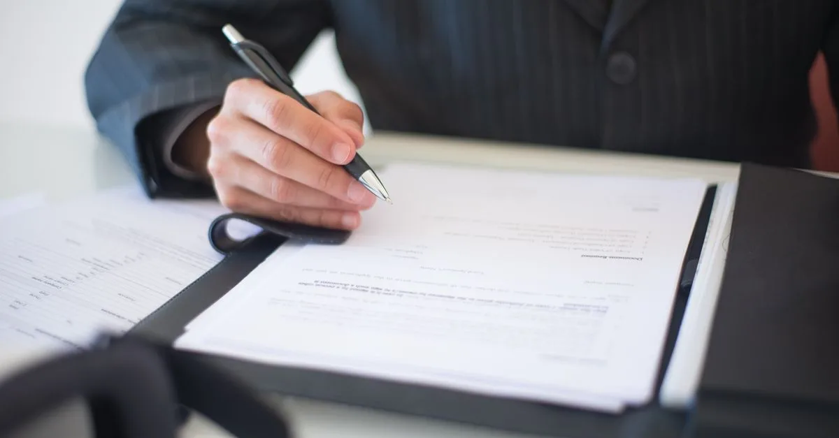 Close-up of a hand signing documents with a pen, symbolizing an important business contract.