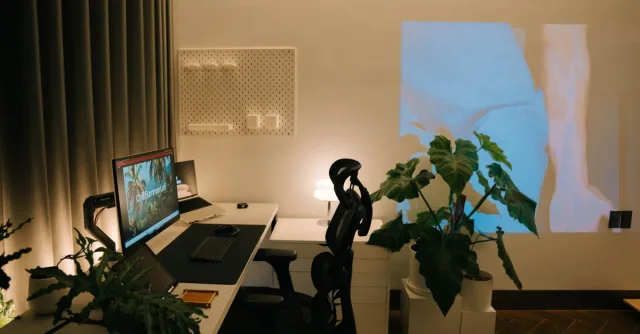 Cozy modern desk setup with plants and a projection on the wall, creating a serene work environment.