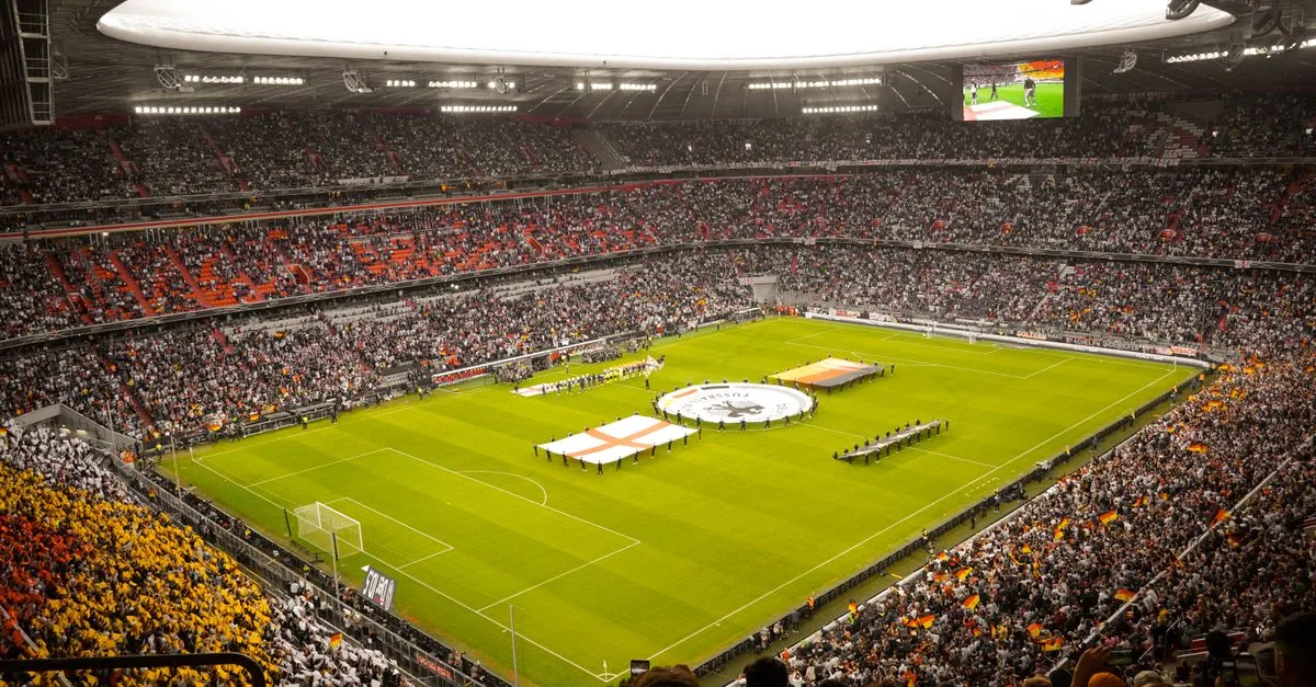 A packed stadium with fans watching a live soccer game, featuring vibrant crowd colors.