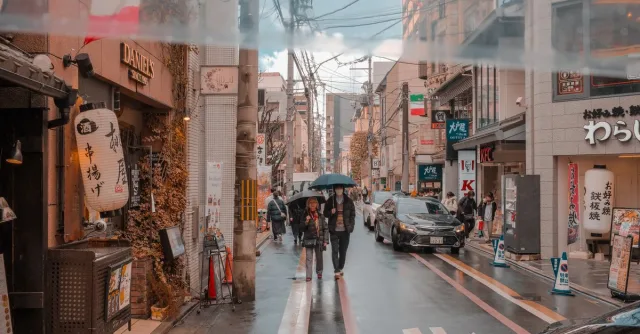 A lively street in Japan with pedestrians and shops under rainy weather.