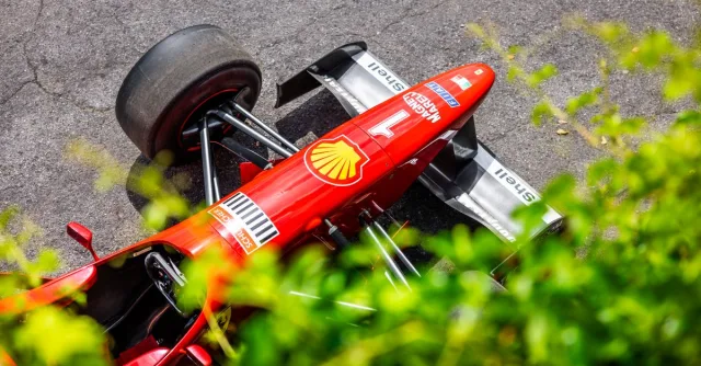 Aerial shot of a red Formula 1 car on a racetrack, surrounded by greenery.