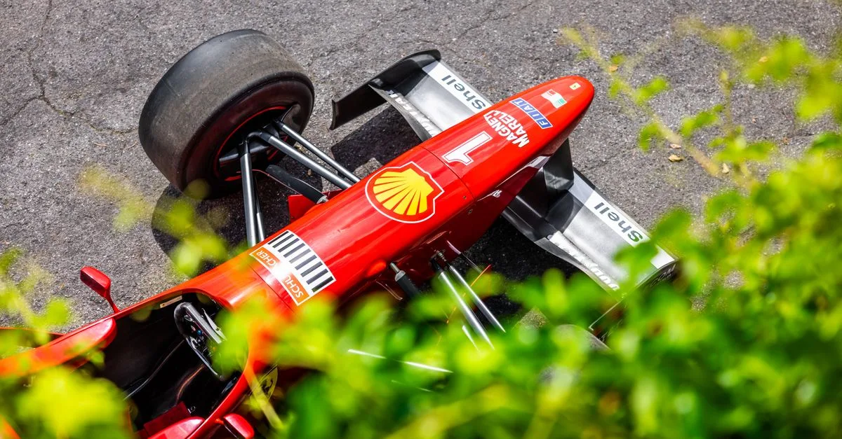 Aerial shot of a red Formula 1 car on a racetrack, surrounded by greenery.