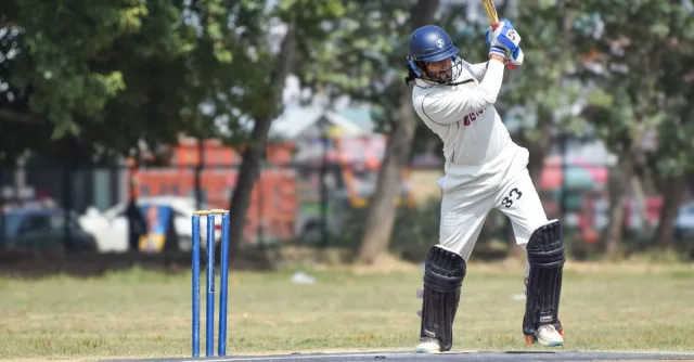 A cricketer in white attire ready to bat on a sunny outdoor field.
