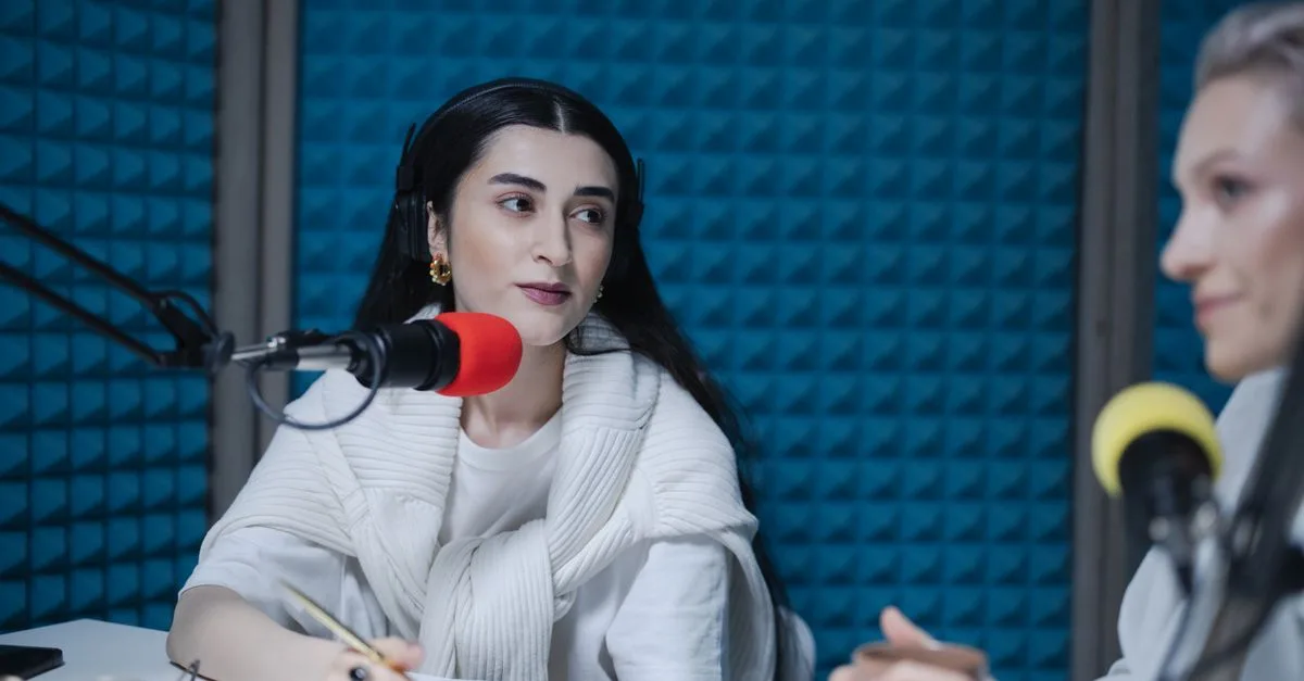 Two women engaged in a podcast recording with professional microphones, soundproof studio.
