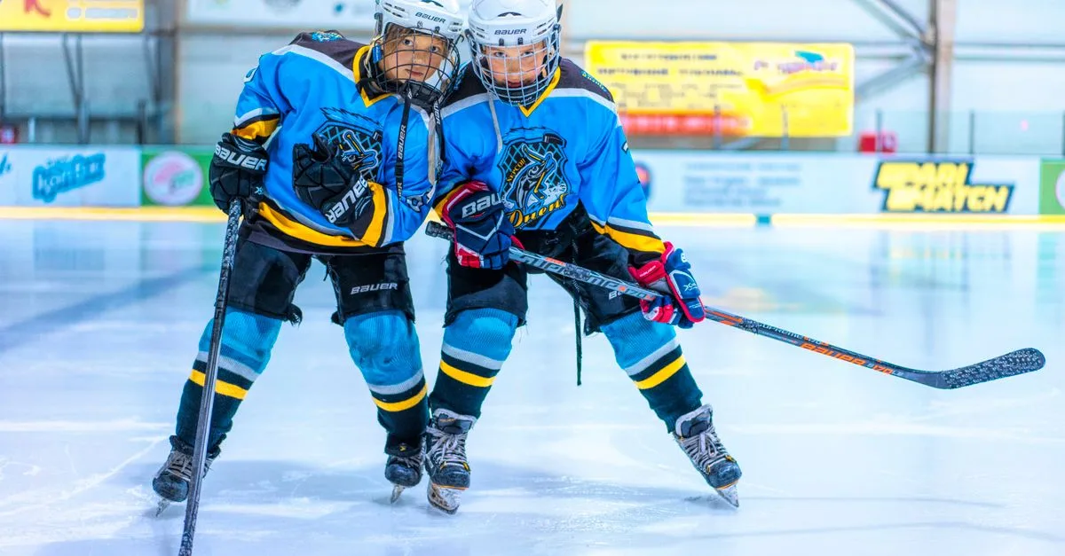 Two female ice hockey players in blue jerseys on a rink, engaged in a game.