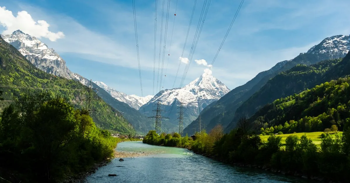 Breathtaking view of the Swiss Alps with a river and lush greenery under a clear blue sky.