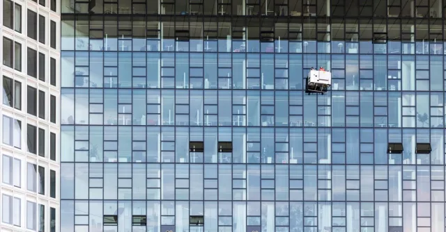High-rise glass building exterior with window cleaners in Hamburg, Germany.