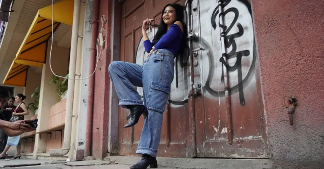 Stylish young woman posing for a street fashion photo shoot in front of graffiti-covered door.