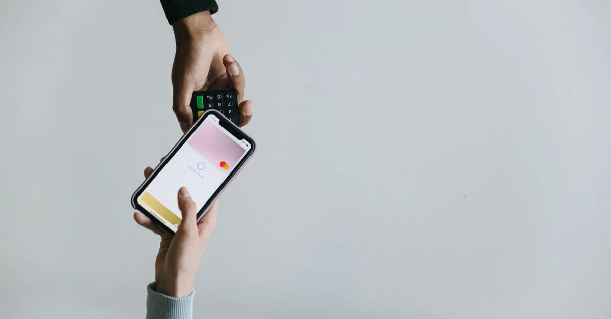Hands using smartphone and terminal for cashless payment, showcasing modern transaction methods.