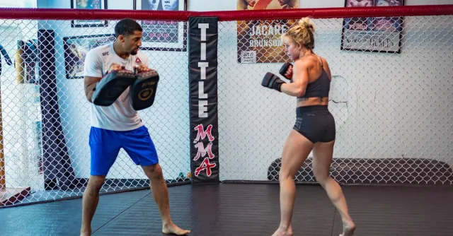 Male instructor trains female MMA athlete in cage gym setting.