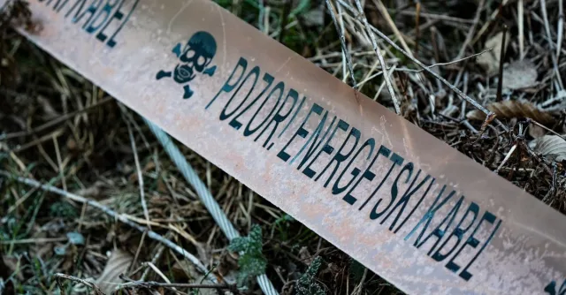 Caution tape reading 'POZOR! ENERGETSKI KABEL' lies on vegetation.